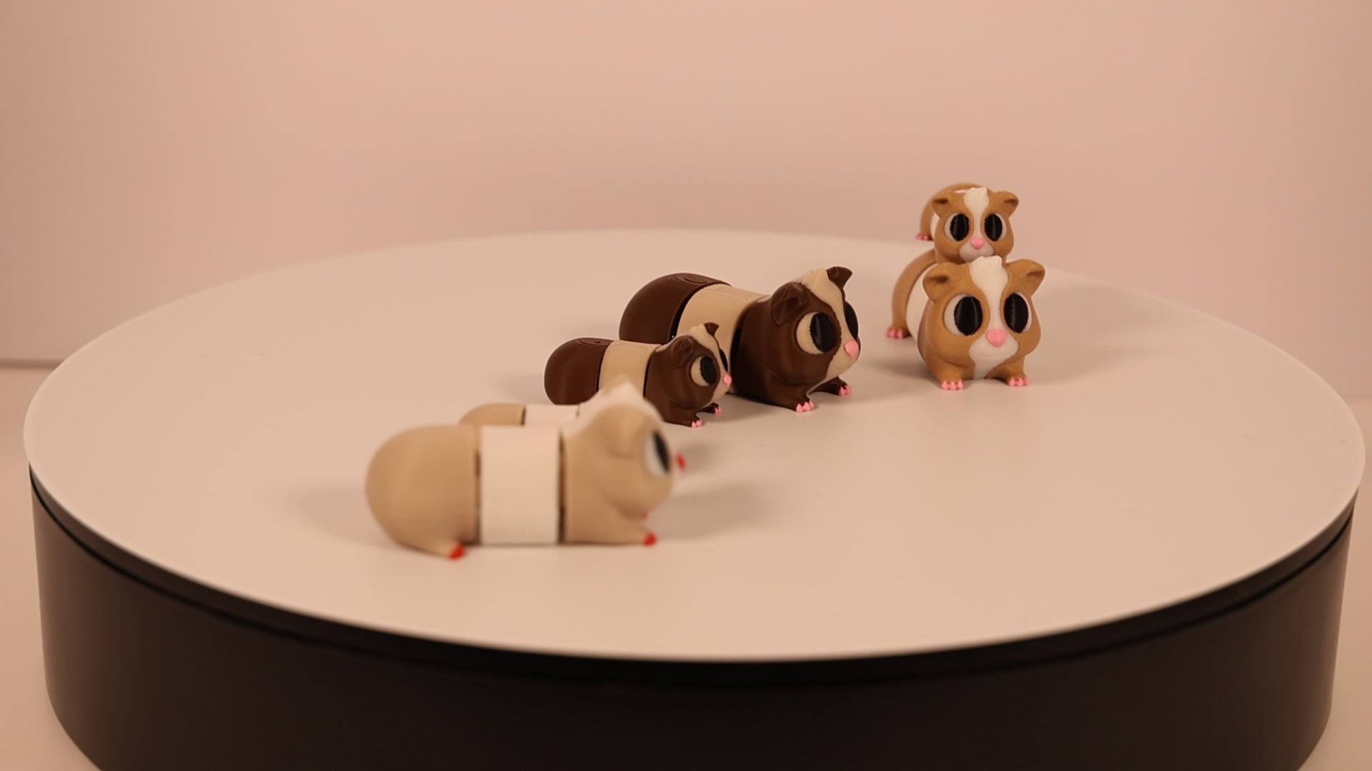 Group of articulated 3D‑printed guinea pig desk pets in multiple colors and sizes moving together.